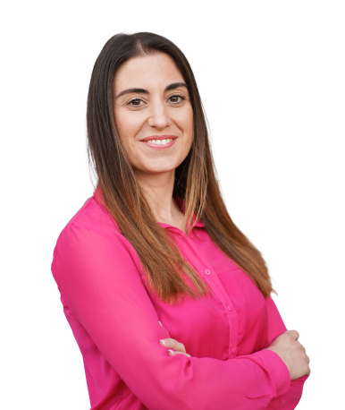 A woman with long hair, smiling and wearing a bright pink blouse, with her arms crossed.